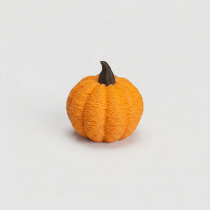 Närbild på en liten orange pumpa på ca 3 cm med texturerad yta, tydliga klyftor och böjd brun stjälk