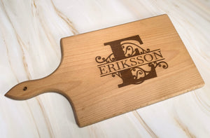 Personlig skärbräda i FSC-certifierat trä med monogram och gravyr – exempel med bokstaven E och texten Eriksson, liggande på ljus yta.