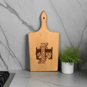 Personlig skärbräda i FSC-certifierat trä med monogram och gravyr – exempel med bokstaven E och texten Eriksson, stående mot ljus bakgrund.