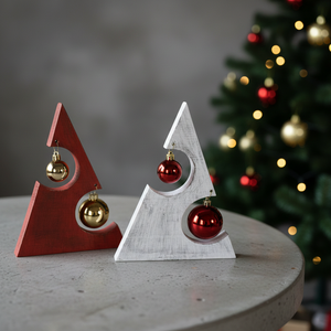 Två rustika handgjorda julgranar på ett bord en röd och en vit, dekorerade med kulor och gran i bakgrunden – handgjorda av Norrgården i Fivelstad.