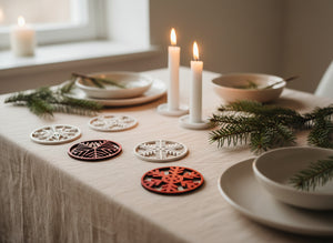 Bordsdekorationer i trä med snöflingor i vitt och rött, placerade på en juldukning med ljus och granris.