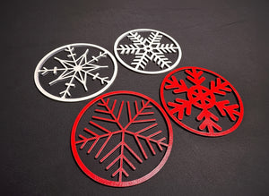 Fyra trädekorationer med snöflingor i rött och vitt, fotograferade mot svart bakgrund.