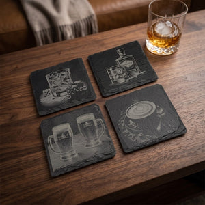 Fyra skifferunderlägg med dryckesmotiv uppställda på ett träbord med whiskyglas.