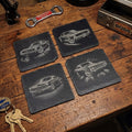 Fyra skifferunderlägg med muskelbilsmotiv uppställda på ett verkstadsbord.