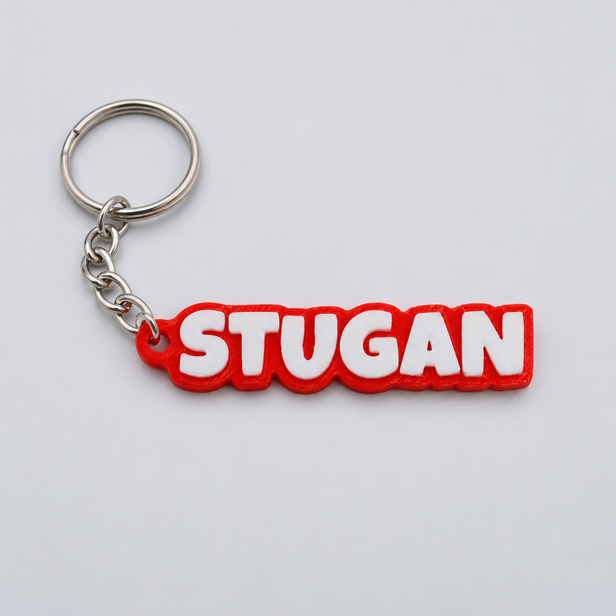 3D-printad nyckelring i TPU med texten STUGAN, vit text på röd bottenplatta