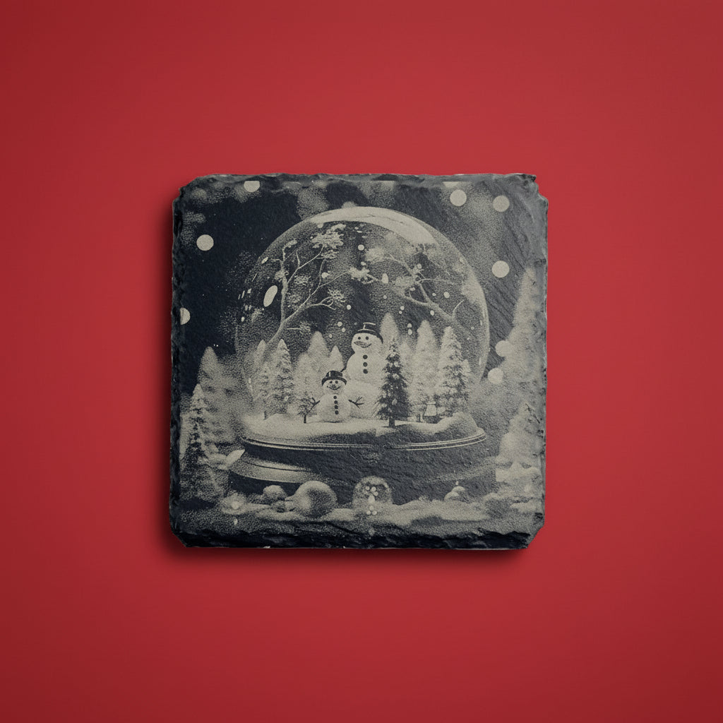 Snöglob med snögubbar och vintermotiv graverad på skifferunderlägg.