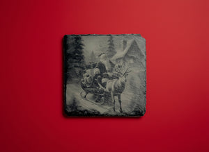 Tomte i släde framför en vinterstuga graverad på skiffer.