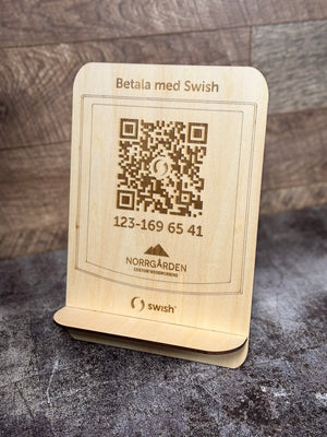 Framsidan av en swishskylt i trä med graverad QR-kod och logotyp